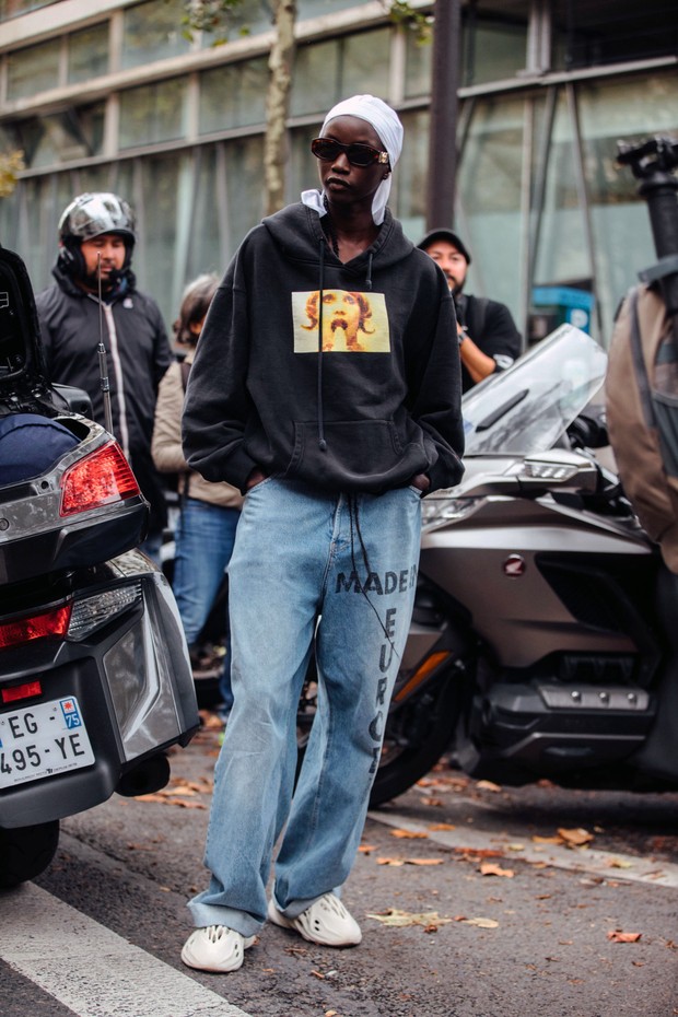PARIS, FRANCE - OCTOBER 03: Model Anok Yai wears a white du-rag, sunglasses, a black hoodie with a photograph, baggy "Made In Europe" jeans and white Yeezy Foam Runner sneakers after the Ann Demeulemeester show on October 03, 2021 in Paris, France. (Photo (Foto: Getty Images)