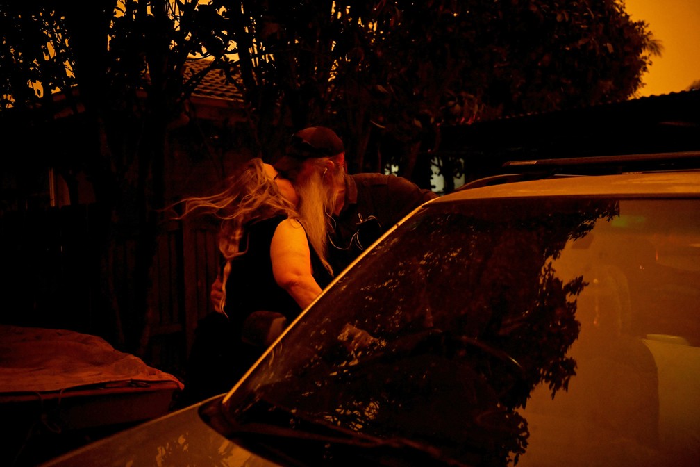 4 de janeiro - Andrea Faulkner dá um beijo de despedida no marido enquanto ela evacua a casa e ele fica para tentar defender dos ataques das brasas enquanto o fortes ventos trazem fumaça e cinzas do incêndio em direção a Nowra, na Austrália — Foto: Tracey  Nearmy/Reuters