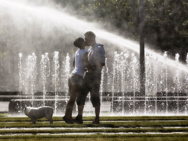Casal se beija em frente a fontes de água enquanto passeiam com cachorro em Berlim, na Alemanha (Foto: Markus Schreiber/AP)