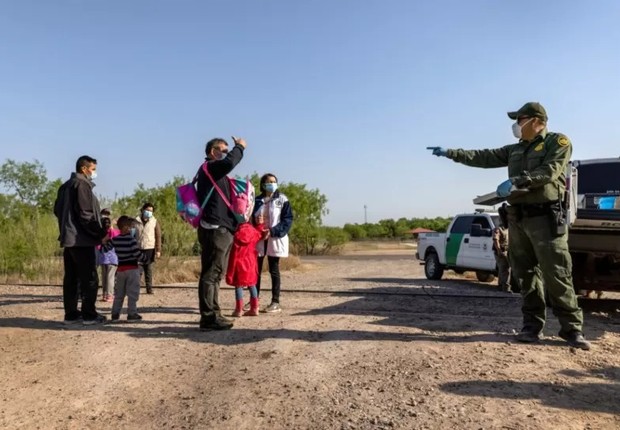 Um agente de patrulha de fronteira dos EUA conversa com uma família venezuelana que atravessou a fronteira do México. A foto foi tirada em 26 de março em Peñitas, Texas (Foto: JOHN MOORE/GETTY IMAGES via BBC)