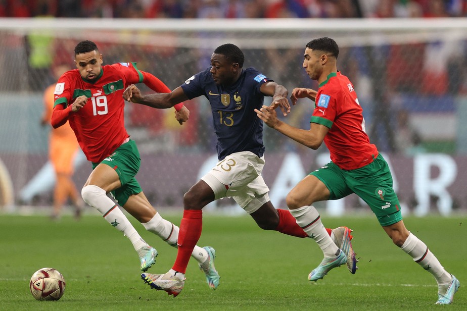 O meio-campista francês Youssouf Fofana arranca com a bola contra o atacante do Marrocos Youssef En-Nesyri e o zagueiro Achraf Hakimi