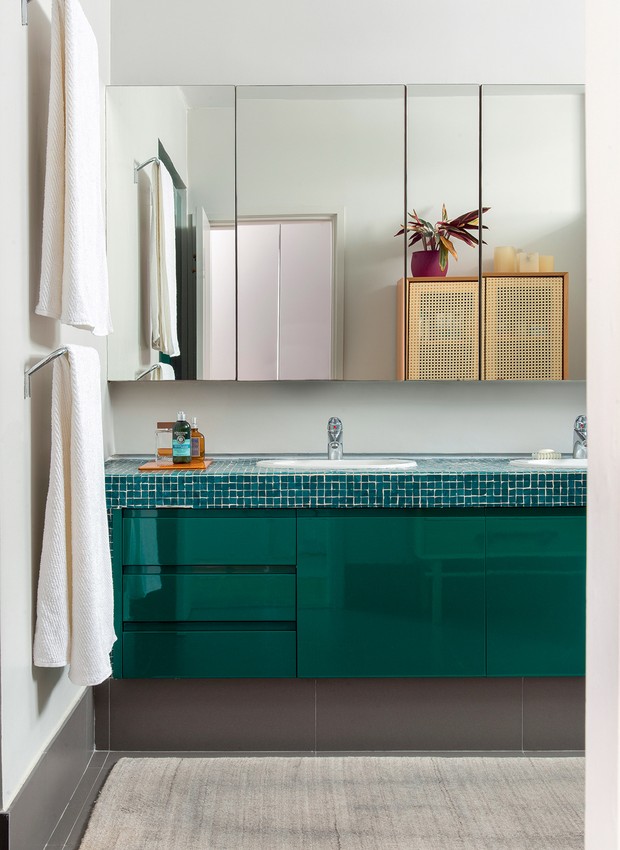 O banheiro do casal tem gabinete da SCA laqueado de verde, que se harmoniza com o tampo revestido de pastilhas de vidro. Os armários espelhados ampliam o ambiente (Foto: Cacá Bratke / Divulgação)