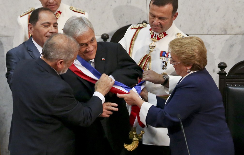 Novo presidente do Congresso chileno Carlos Montes e Michelle Bachelet arrumam faixa presidencial em Sebastián Piñera durante cerimônia de posse neste domingo (11) (Foto: Esteban Felix/ AP Photo)