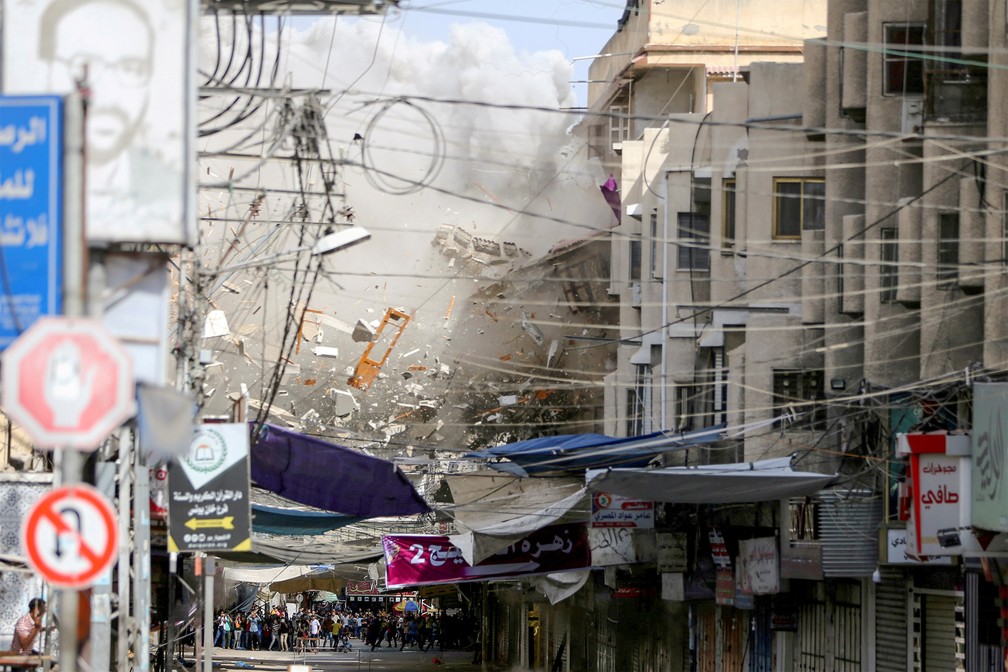 20 de maio - Destroços de prédios caem do alto enquanto pessoas observam ao fundo no momento de um bombardeio israelense contra palestinos em Khan Younis, no sul da Faixa de Gaza — Foto: Ibraheem Abu Mustafa/Reuters