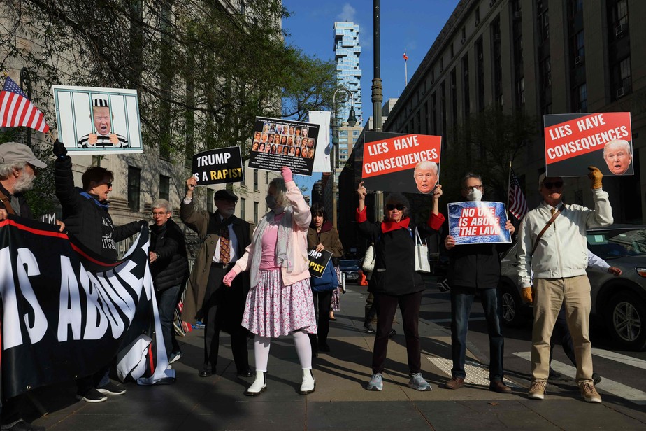 Manifestantes protestam com fotos de Donald Trump em frente ao tribunal em que caso de estupro começou a ser julgado.