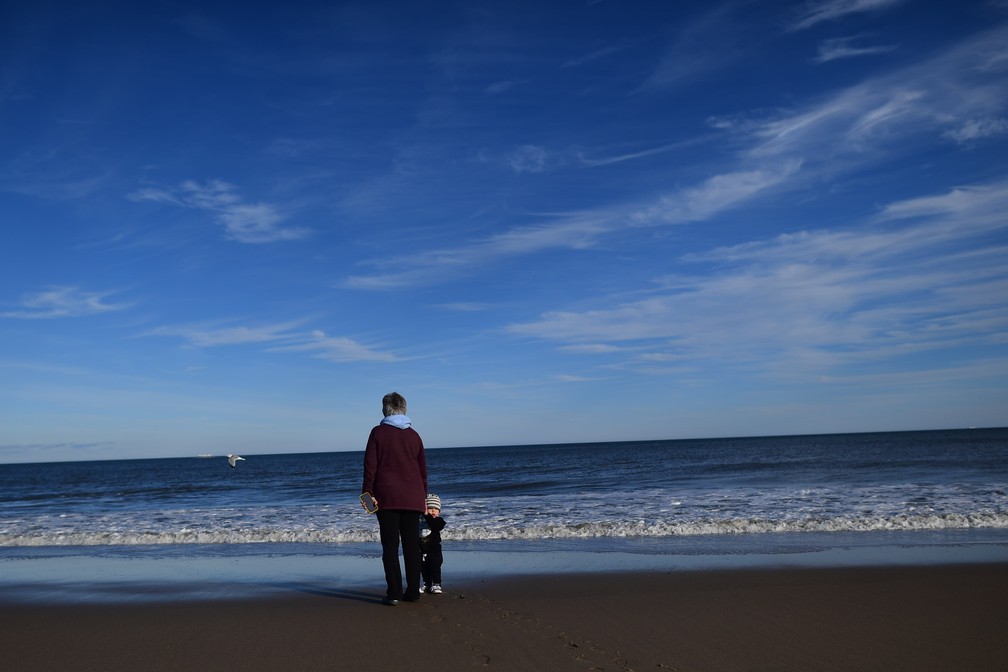 Mulher anda com neto na praia em Delaware, nos Estados Unidos, no dia 2 de janeiro. Estado é banhado pelo Oceano Atlântico. — Foto: Mark Makela/AFP
