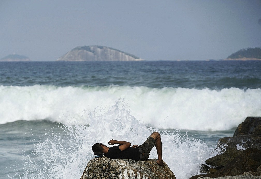 Homem deitado nas pedras da Praia do Leblon durante ressaca em maio de 2022 — Foto: Marcos Serra Lima/g1