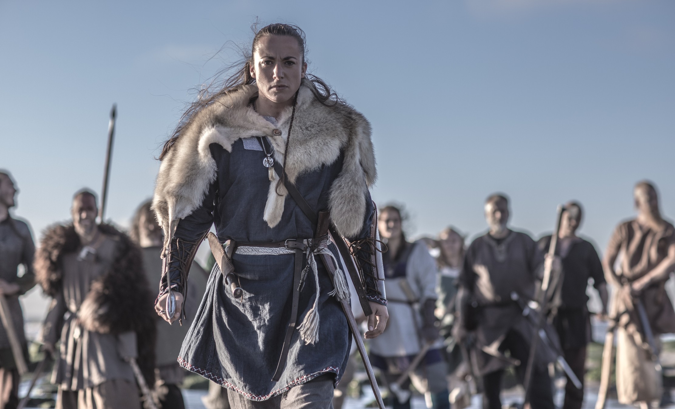 An individual female viking posing in front of a group of warriors stood in the surf on the shore (Foto: Getty Images)
