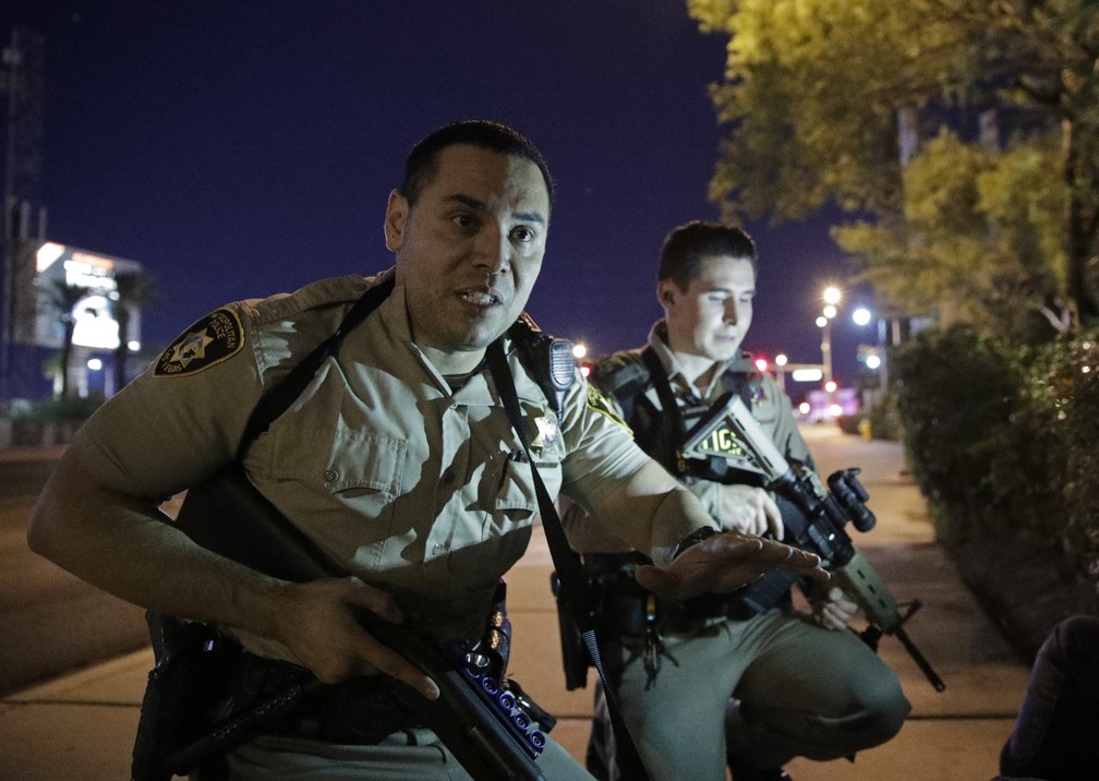 Policiais pedem para pessoas se protegerem perto de local em que tiros foram ouvidos em Las Vegas (Foto: John Locher/AP)