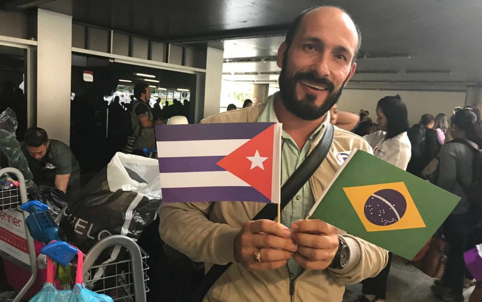 Médico cubano Yoendri Veras segura bandeiras de Cuba e Brasil, no Aeroporto de Brasília, antes de embarcar de volta a Havana — Foto: Marília Marques/G1
