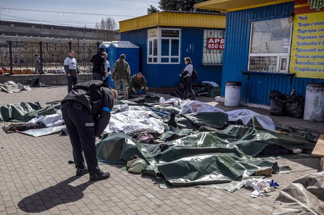 Policial ucraniano observa corpos cobertos após ataque russo a estação de trem em Kramatorsk, usada como rota de saída para civis