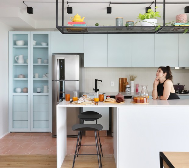 O escritório Studio 92 Arquitetura projetou a cozinha com armários em tom romântico que contrasta com a prateleira suspensa preta em serralheria e a madeira do piso (Foto: Mariana Orsi / Divulgação)