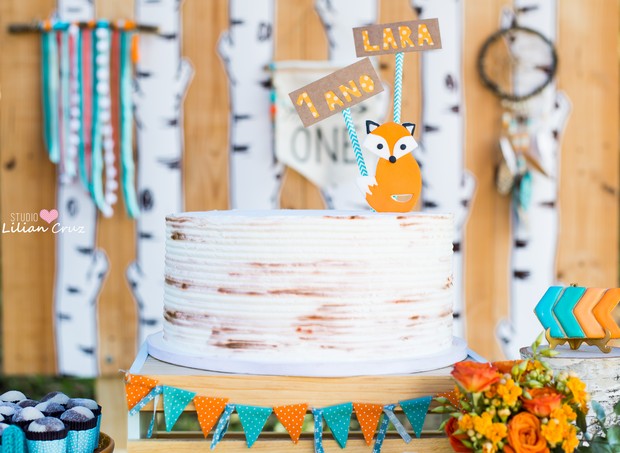O bolo que tem o aspecto de casca de árvore, tem uma raposinha com o nome e a idade da aniversariante no topo e retalhos nas cores da festa na base (Foto: Divulgação / Lilian Cruz)