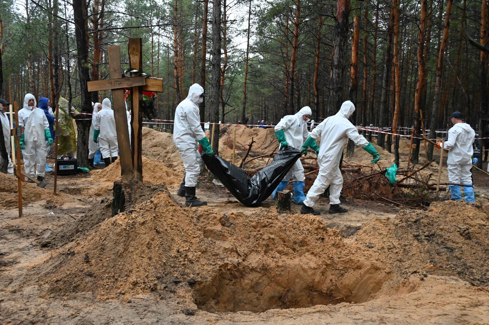 Investigadores carregam um saco de corpos em uma floresta perto de Izium, leste da Ucrânia. — Foto: SERGEY BOBOK / AFP