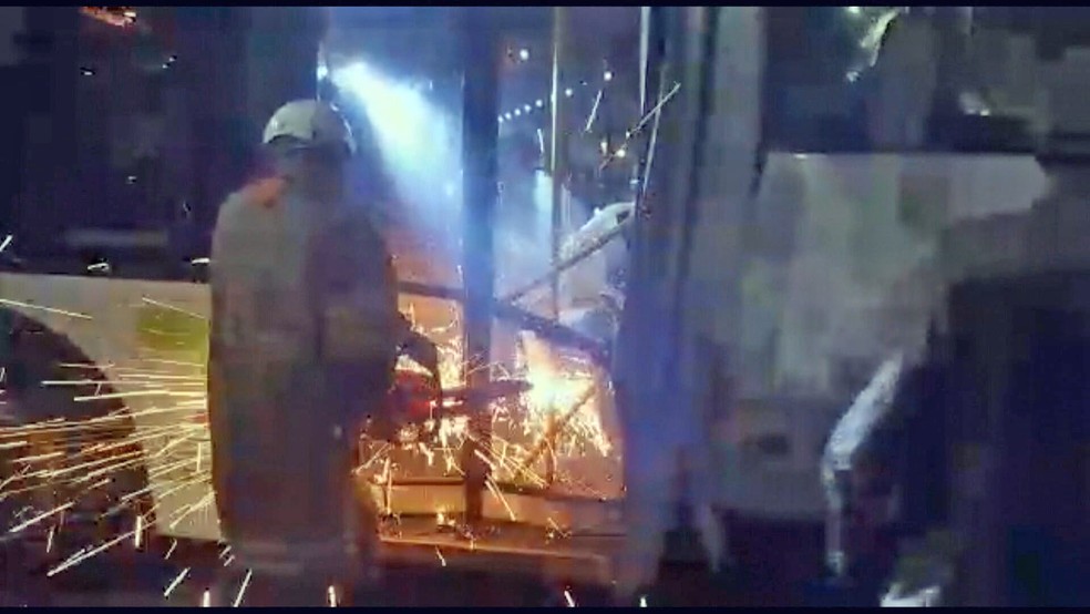 Bombeiro serra porta para resgatar motorista ap&oacute;s batida de &ocirc;nibus &mdash; Foto: Reprodu&ccedil;&atilde;o/TV Globo