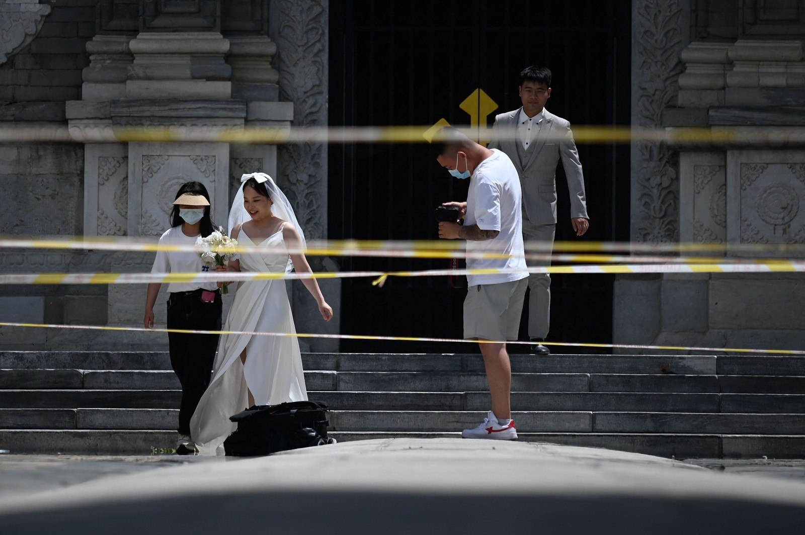 Casal passa pela área isolada enquanto se prepara para tirar fotos do casamento em meio à pandemia de Covid-19, em Pequim.  — Foto: WANG Zhao / AFP