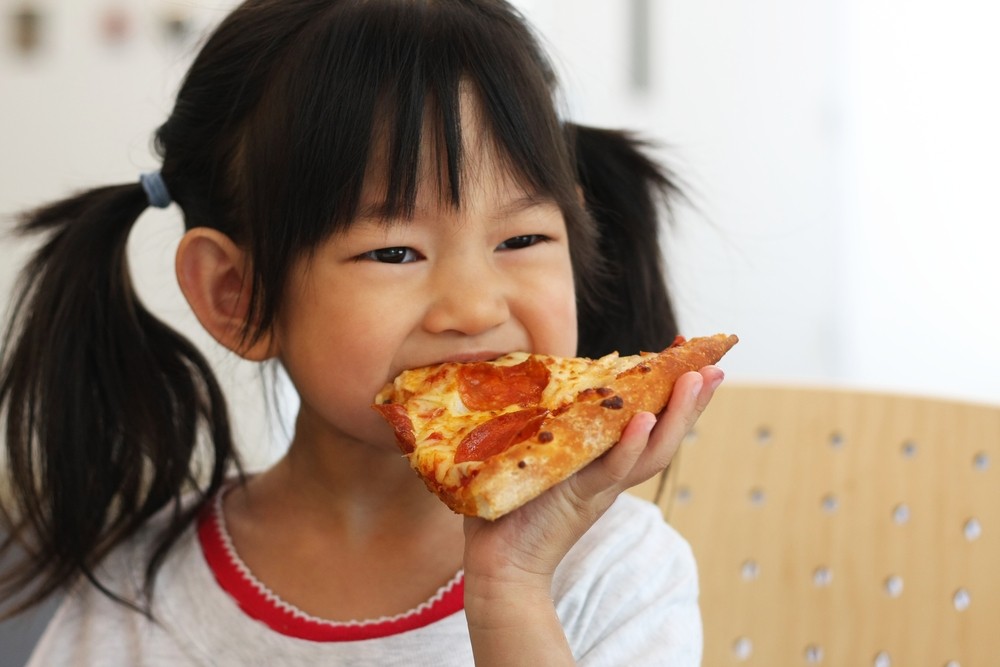 Criança comendo um pedaço de pizza (Foto: Shutterstock)