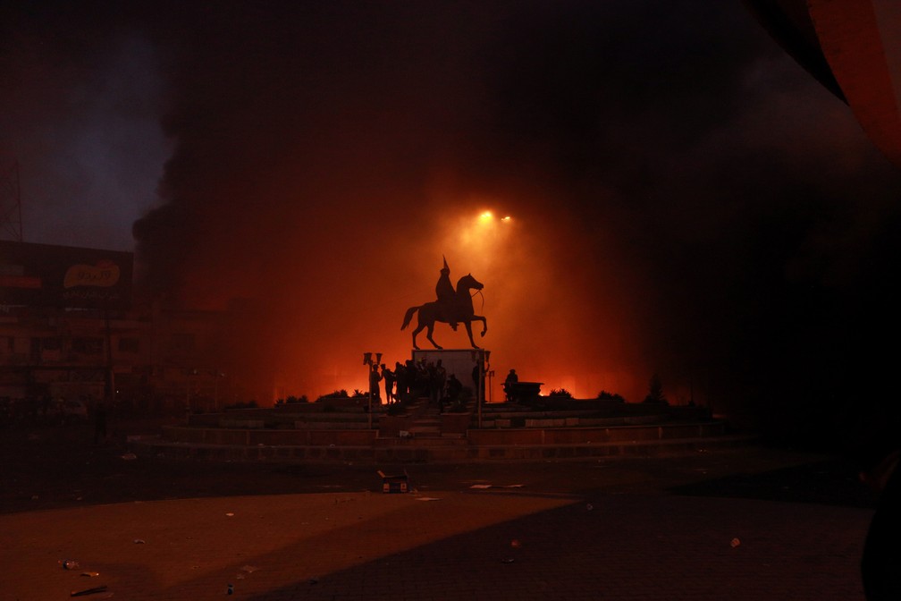 4 de novembro - Manifestantes contra o governo colocam fogo enquanto forças de segurança disparam tiros e bombas de gás lacrimogêneo perto de uma estação de TV estatal em Bagdá, no Iraque — Foto: Hadi Mizban/AP