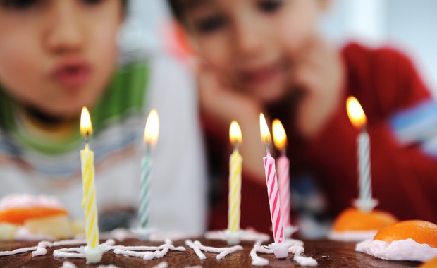 Crianças assoprando vela de bolo de aniversário em festa (Foto: Shutterstock)