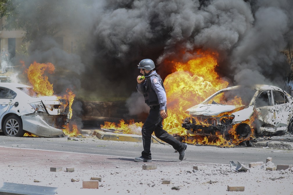Bombeiro israelense caminha ao lado de carros atingidos por míssil disparado da Faixa de Gaza, na cidade de Ashkelon, no sul de Israel, em 11 de maio de 2021 — Foto: Ariel Schalit/AP