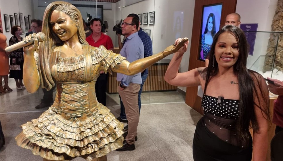 Irmã de Paulinha Abelha ao lado de escultura da cantora — Foto: Arquivo Pessoal