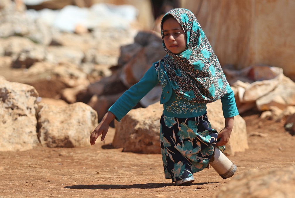 20 de junho â Maya Mohammad Ali Merhi, de 8 anos, caminha usando protÃ©ses nas pernas feitas pelo seu pai com latas, em um campo para desabrigados na provÃ­ncia sÃ­ria de Idlib. Maya e seu pai nasceram sem membros inferiores. Incapaz de arcar com prÃ³teses reais, seu pai fez um par de latas cheias de algodÃ£o e pedaÃ§os de pano â Foto: Aaref Watad/AFP