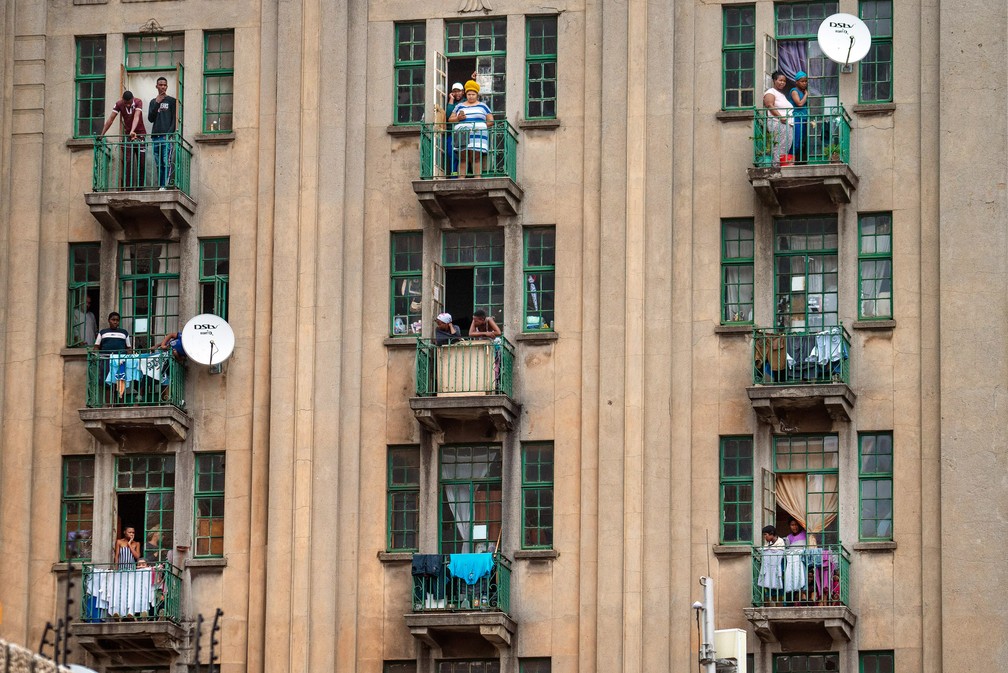 Moradores assistem de suas varandas a polícia e as forças de defesa nacional revistarem um bar por suspeita de estar aberto ilegalmente no centro de Joanesburgo, na África do Sul, em 30 de março. O país entrou em um bloqueio nacional por 21 dias para controlar a propagação do novo coronavírus  — Foto: Jerome Delay/AP