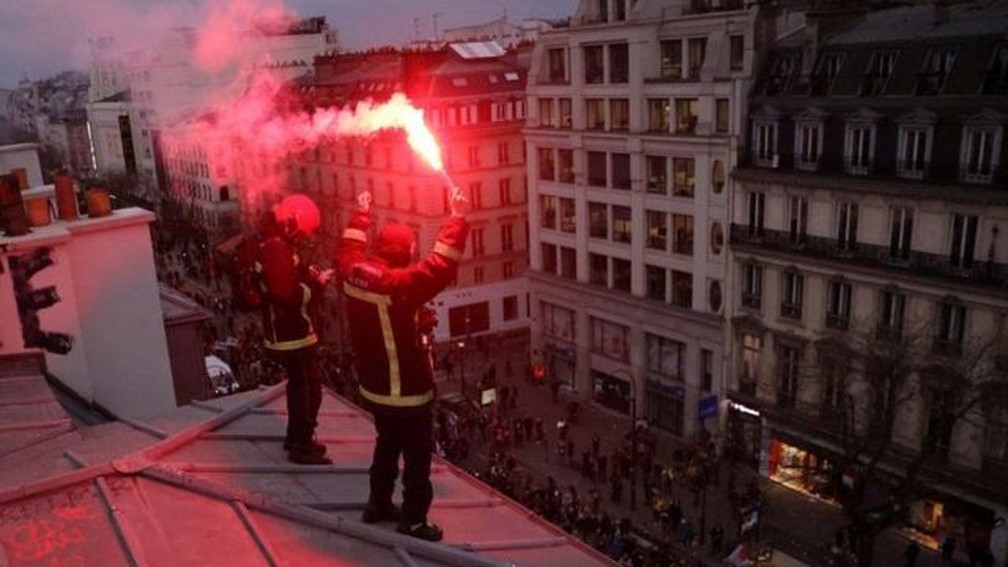 Bombeiros em greve no telhado de um prédio em Paris durante os protestos de quinta-feira — Foto: Reuters via BBC