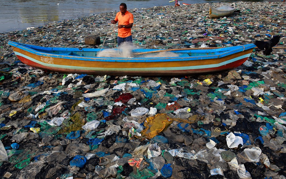Um pescador prepara a sua rede nas margens do Mar Arábico, cheio de sacos de plástico, em Mumbai, na Índia.  — Foto:  Rafiq Maqbool/AP