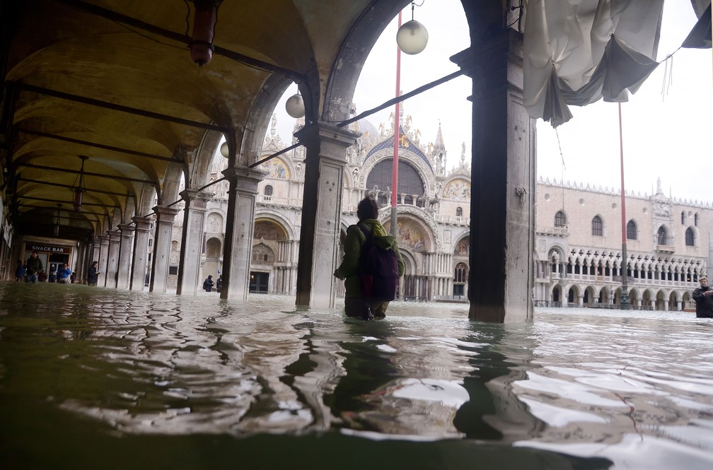 Pessoa atravessa uma arcada inundada perto da Basílica de San Marco, em Veneza, na Itália, nesta sexta-feira (15)  — Foto: Filippo Monteforte / AFP