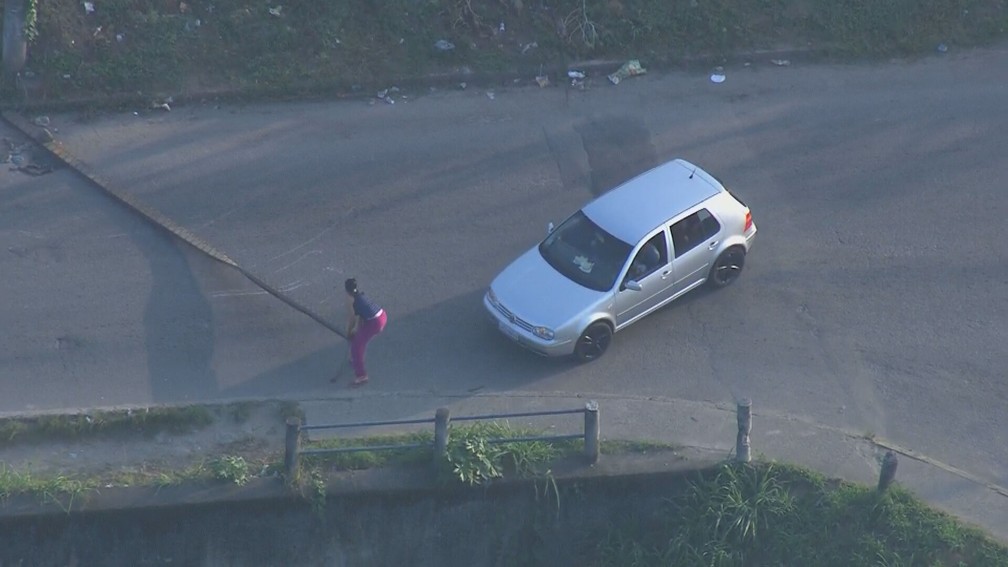 Mulher precisa descer do carro para retirar barricada colocada por criminosos em rua da Vila Aliança  — Foto: Reprodução / TV Globo