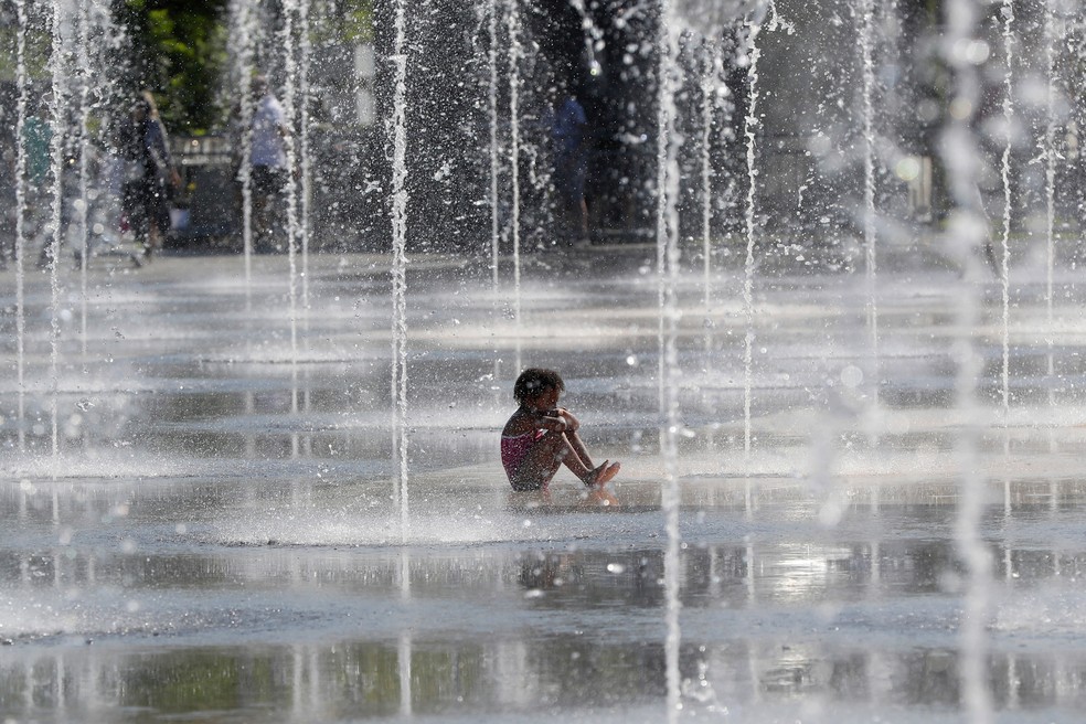 Uma criança senta em uma fonte de água durante um dia quente de verão em Nice, no sudoeste da França (Foto: Valery Hache/AFP)