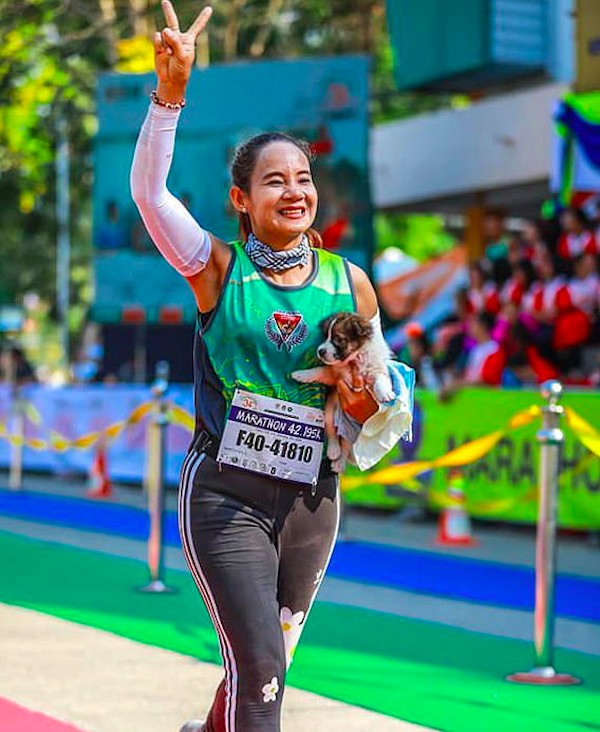 A corredora Khemjira Klongsanun cruzando a linha de chegada da maratona na Tailândia com o cachorrinho encontrado por ela no colo (Foto: Twitter)