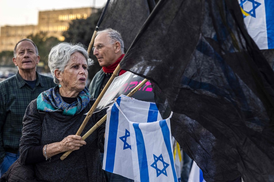 Ativista de esquerda agita bandeiras pretas e israelenses durante protesto contra a coalizão de Netanyahu perto do Knesset em Jerusalém