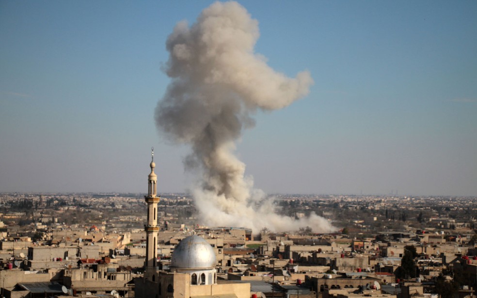 Fumaça é vista em prédios atingidos por bombardeio na vila de Mesraba, na região de Guta Oriental, após bombardeio na segunda-feira (19) (Foto: Hamza Al-Ajweh / AFP)