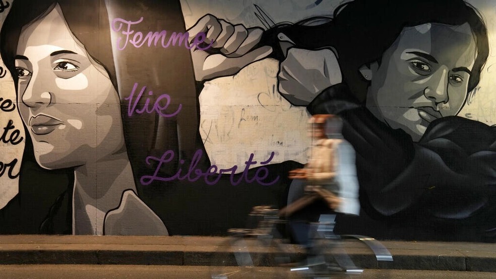 Um homem anda de bicicleta na frente de um mural, em um túnel de Paris, que retrata mulheres cortando o cabelo para mostrar apoio aos manifestantes iranianos. A população do Irã enfrenta o regime de Teerã após a morte de uma jovem sob custódia policial — Foto: AP - Francois Mori