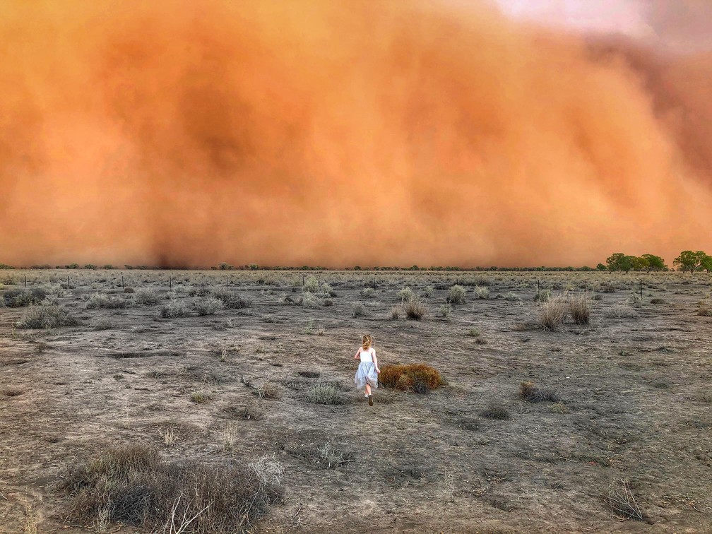 Na foto, tirada no dia 17 de janeiro, uma menina corre em direção a uma tempestade de poeira em Mullengudgery, estado de Nova Gales do Sul, no sudeste australiano. — Foto: Handout / Courtesy of Marcia Macmillan / AFP