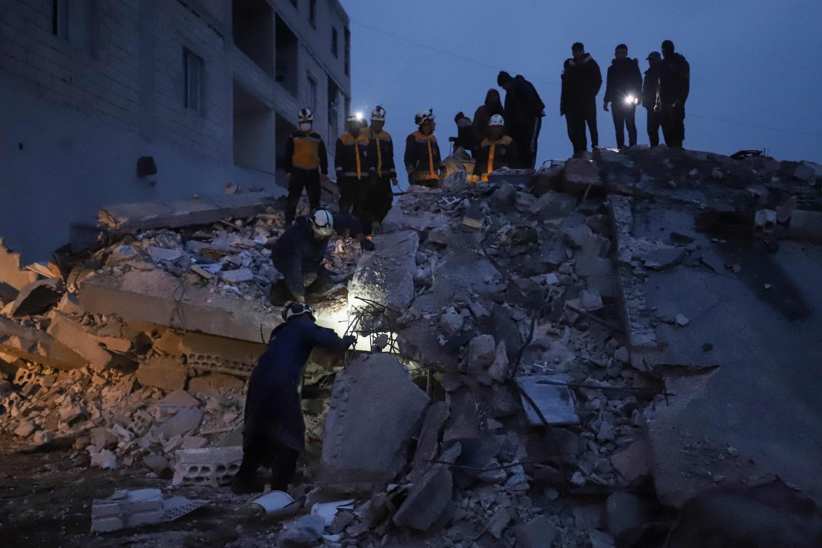 Membros da defesa civil síria, conhecidos como Capacetes Brancos, procuram vítimas nos escombros após terremoto em 6 de fevereiro de 2023 — Foto: Abdulaziz Ketaz / AFP