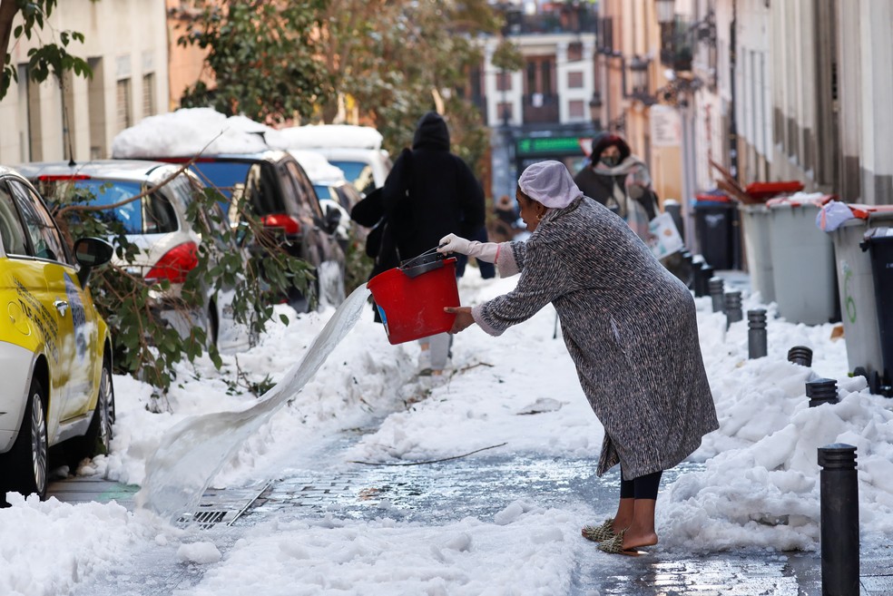 Mulher joga água em rua e calçada cobertas de gelo após forte nevasca em Madrid, capital da Espanha, nesta segunda-feira 11 de janeiro de 2021 — Foto: Susana Vera/Reuters
