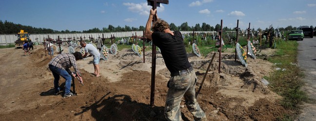 Trabalhadores comunitários enterram caixões durante funeral coletivo de pessoas não identificadas mortas no bimestre fevereiro-março de 2022 no cemitério de Bucha, Ucrânia  — Foto: SERGEI CHUZAVKOV / AFP