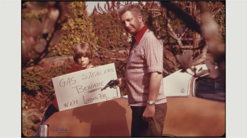 Um homem com uma arma e um sinal alertando contra o roubo de combustível nos anos 1970 (Foto: US National Archives via BBC News)