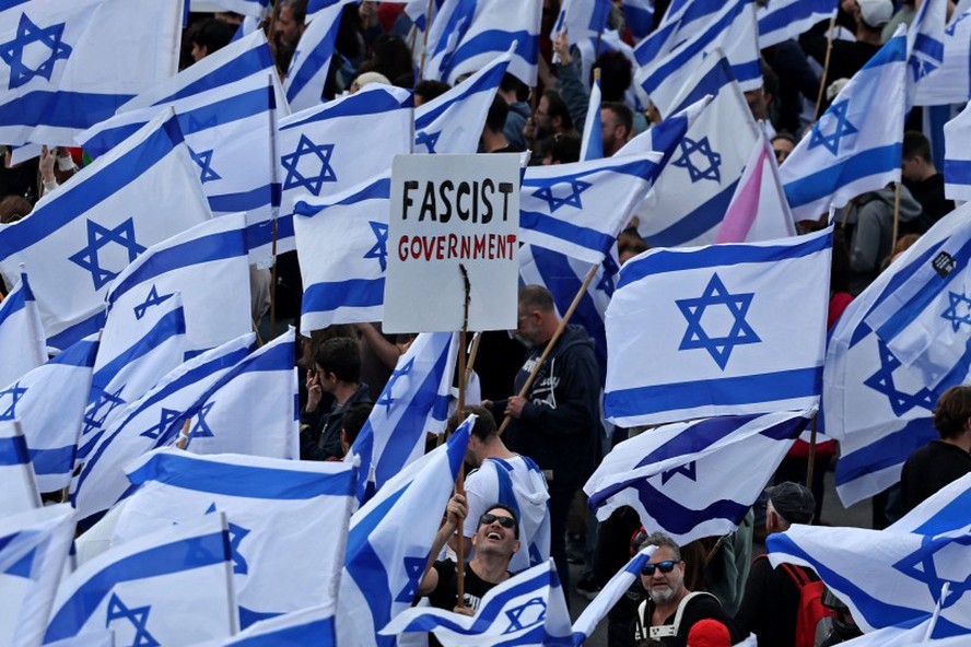 Em Jerusalém, manifestante carrega cartaz com a frase 'governo fascista' em meio a bandeiras de Israel