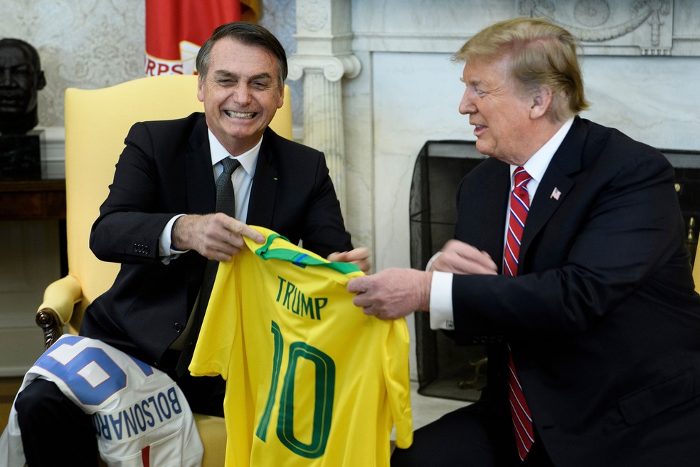 O presidente Jair Bolsonaro entrega camisa da SeleÃ§Ã£o Brasileira de futebol para Donald Trump; presidente norte-americano tambÃ©m presenteou Bolsonaro â€” Foto: Brendan Smialowski / AFP