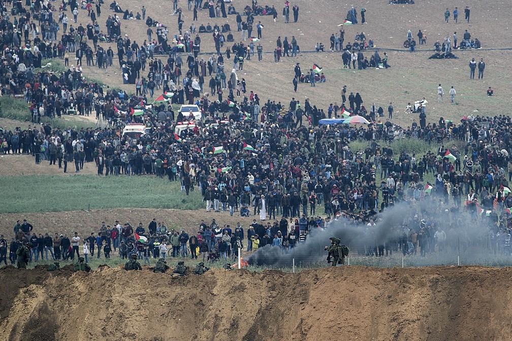 Soldados israelenses e manifestantes palestinos são vistos na fronteira da Faixa de Gaza com Israel nesta sexta-feira (30) (Foto: Tsafrir Abayov/AP Photo)