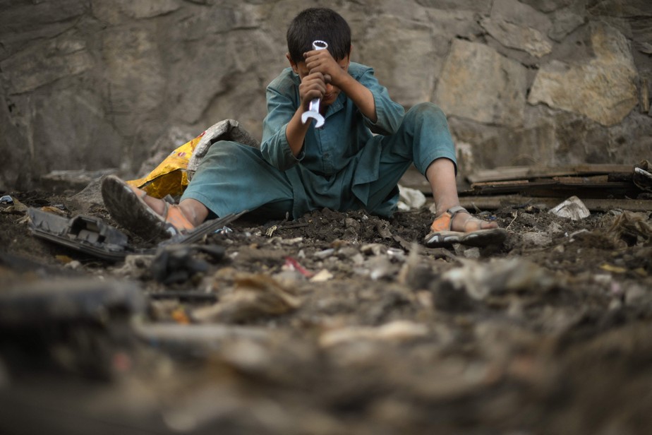 Criança usa uma chave inglesa enquanto procura sucata em Cabul, Afeganistão