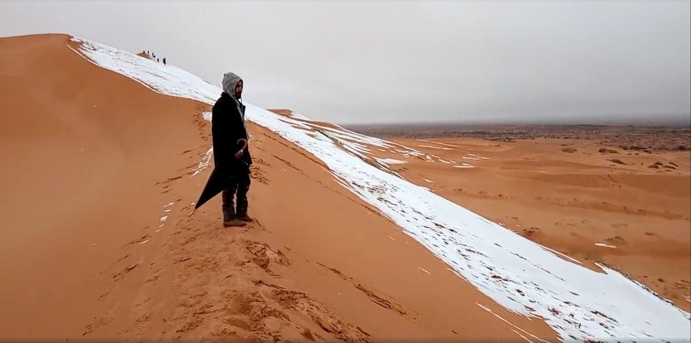 Homem olha para duna coberta de neve no deserto do Saara, na cidade de Ain Sefra, Argélia (Foto: Hamouda Ben Jerad/via Reuters)