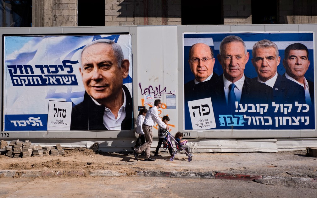 Israelenses passam por cartazes do primeiro-ministro Benjamin Netanyahu, líder do Likud, e dos candidatos do partido Azul e Branco, Moshe Yaalon, Benny Gantz, Yair Lapid e Gabi Ashkenazi, em Tel Aviv, na quarta-feira (3) — Foto: AP Photo/Oded Balilty