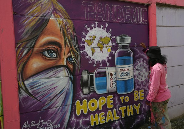 Mulher termina mural que mostra vacina contra a Covid-19 ao lado de um rosto de máscara em Jakarta, na Indonésia, nesta segunda-feira (8). — Foto: Demy Sanjaya / AFP