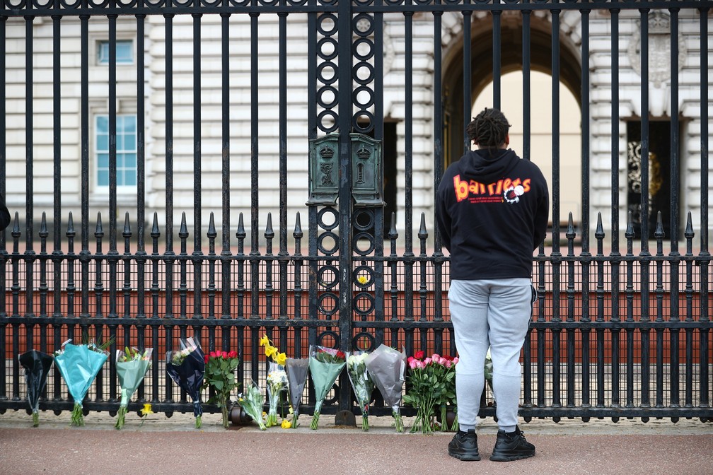 Pessoa presta homenagem ao lado de buquês de flores no portão do Palácio de Buckingham, em Londres, após o anúncio da morte do príncipe Philip, marido da rainha Elizabeth II, em 9 de abril de 2021 — Foto: Hannah McKay/Reuters