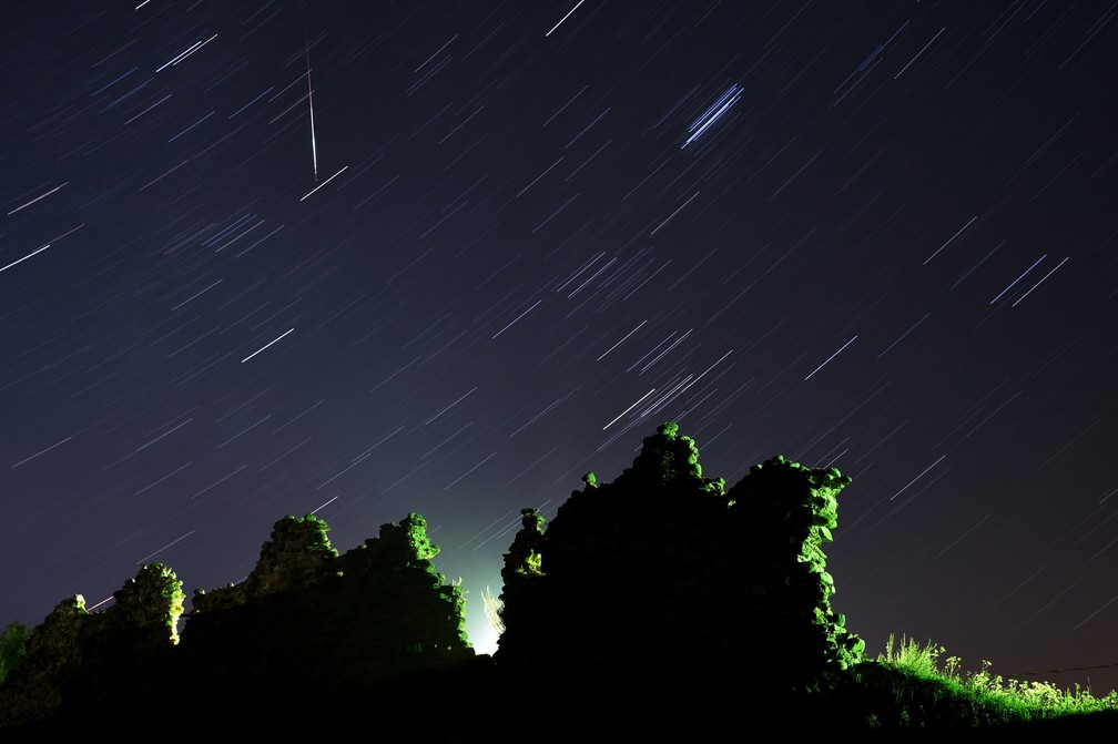 Foto tirada com longa exposição mostra um meteoro Perseid cruzando o céu na vertical e o rastro das estrelas acima das ruínas de um castelo medieval na vila de Kreva, a cerca de 100 km a noroeste de Minsk, na Bielorrússia  — Foto: Sergei Gapon/AFP
